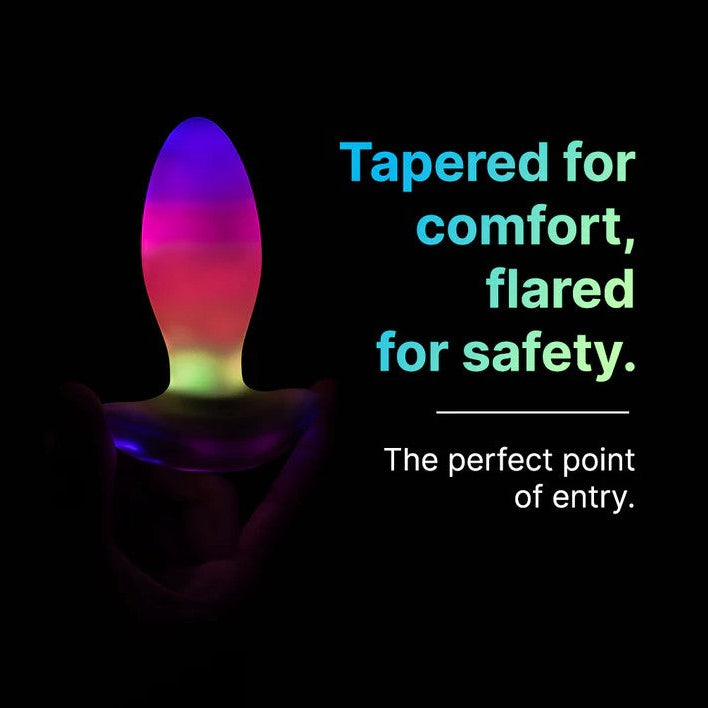 White tapered butt plug with a flared base, glowing vibrant LED colors of purple, pink, and green.