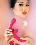 A woman smiling while holding a Jimmyjane Reflexx Rabbit 3 First Time Slim Flexible Warming Vibrator - Pink, partially submerged in a milky bath with rose petals.