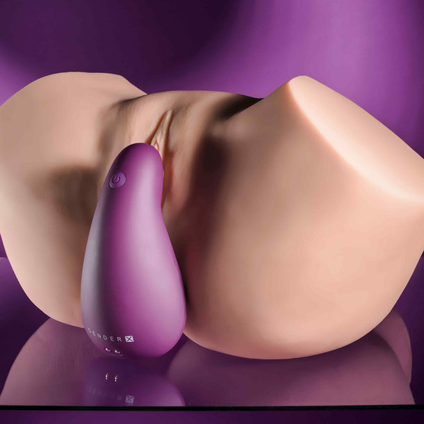 Purple silicone BJ Buddy compact vibrator on a peach-toned anatomical model, enhancing oral play.