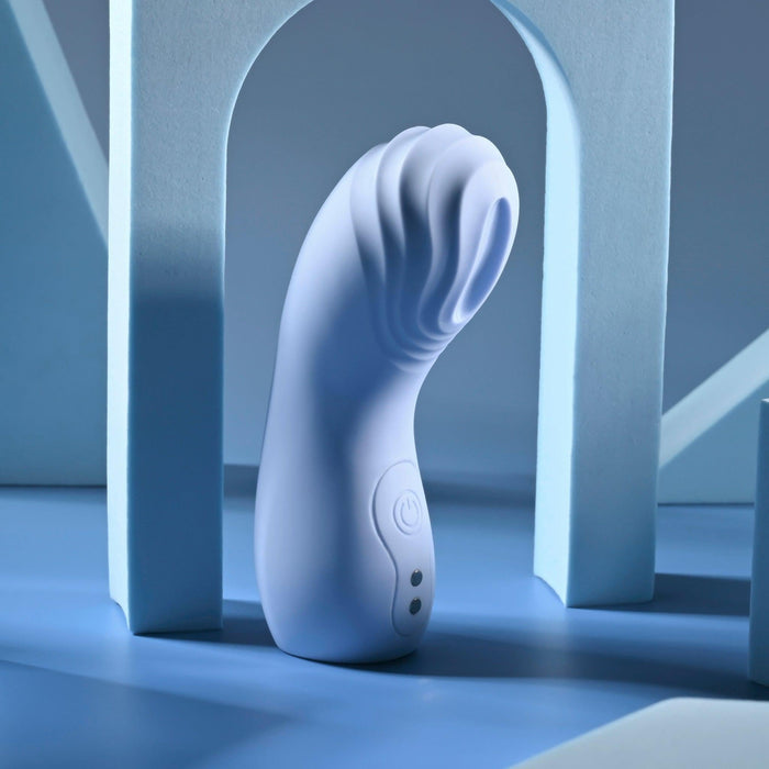 The Good Point G Spot Finger Vibrator, a sleek and modern white device with a curvy design reminiscent of a waterproof vibrator, stands upright against blue geometric shapes. It has a textured grip and side buttons, hinting at electronic functionality in a minimalist, stylish setting.