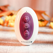The Velvet Hammer Thrusting Hands-Free Dual Stimulation Vibrator is an oval-shaped waterproof silicone toy with a white body, three purple buttons (+, power, -), and "GENDER X" printed at the base, standing upright on a light surface.