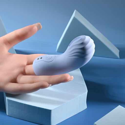 A hand holds the compact Good Point G Spot Finger Vibrator, which is pale blue with a curved, textured design ideal for g-spot pleasure. The background highlights geometric blue shapes, adding a modern minimalist touch.