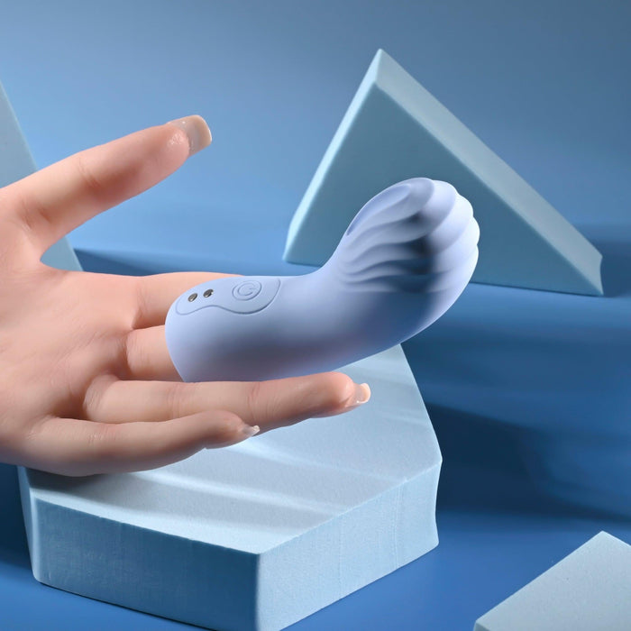A hand holds the compact Good Point G Spot Finger Vibrator, which is pale blue with a curved, textured design ideal for g-spot pleasure. The background highlights geometric blue shapes, adding a modern minimalist touch.