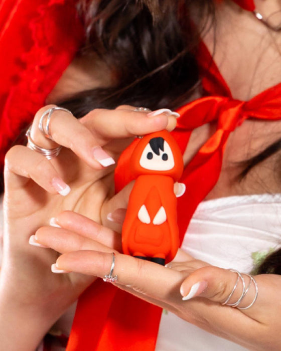 A person with manicured nails and silver rings holds the Little Red Discreet Powerful Bullet Vibrator—a small, red, hooded figure with black hair, white eyes, and a white top with a red ribbon—crafted from smooth silicone.