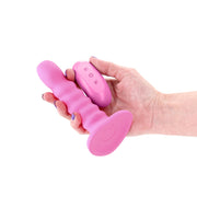 Pink ribbed silicone vibrating dildo with a suction cup base and a matching remote control held in a hand.
