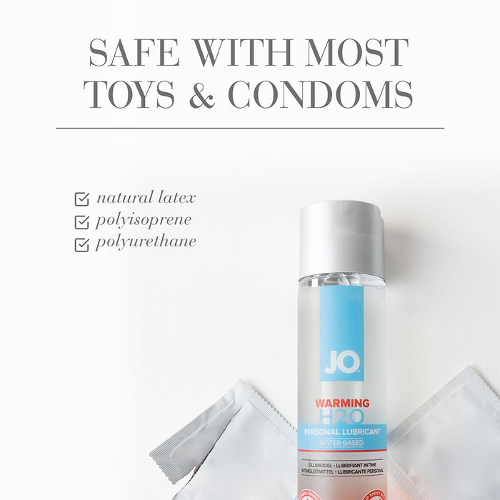A bottle of Jo H2O Warming Water Based Lubricant stands upright beside two unwrapped condoms on a white surface. Above, text reads: "SAFE WITH MOST TOYS & CONDOMS" and checks off natural latex, polyisoprene, and polyurethane.