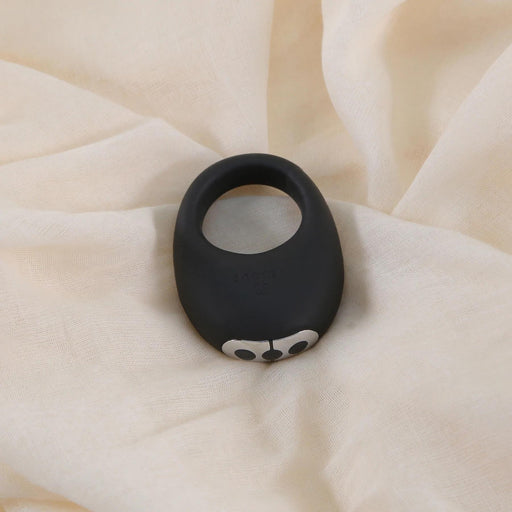 A Je Joue Mio Vibrating Cock Ring - Black, featuring two white eye-like designs, is displayed on a soft cream-colored fabric background.