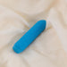The Je Joue Powerful Classic Bullet with Finger Sleeve in teal, a USB rechargeable vibrator with a rounded tip, rests on cream fabric, ready to deliver rumbly sensations.