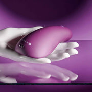 Smooth, compact purple vibrator held in a white hand, reflecting on a purple surface.