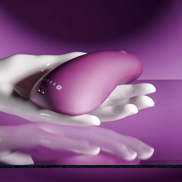 Smooth, compact purple vibrator held in a white hand, reflecting on a purple surface.