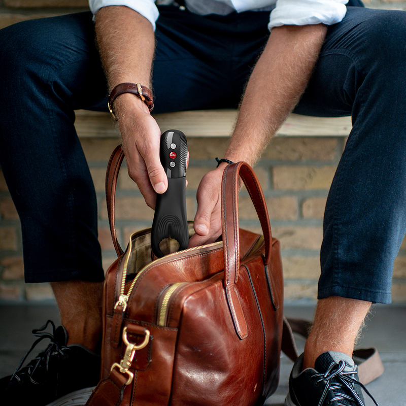 Man placing a black Fun Factory Manta vibrating penis stroker with red buttons into a brown leather bag.