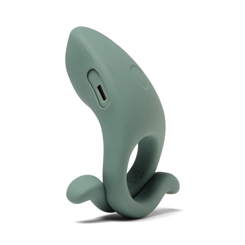 The Dame Hug Adjustable Vibrating Cock Ring for Couples is a green silicone ring with a curved ergonomic design, circular base, raised tail-like extension, and side charging port, shown against a white background.