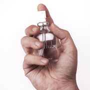A hand presses the white nozzle of a 50 ml UberLube Premium Silicone Lubricant bottle, labeled "lube," highlighting its long-lasting formula against a plain white background.