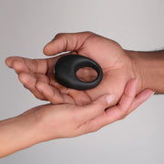 Someone places the Je Joue Mio Vibrating Cock Ring - Black into another person’s open palm, set against a neutral background.