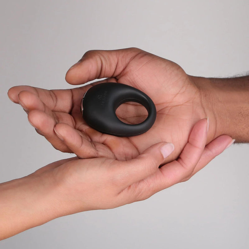 Someone places the Je Joue Mio Vibrating Cock Ring - Black into another person’s open palm, set against a neutral background.