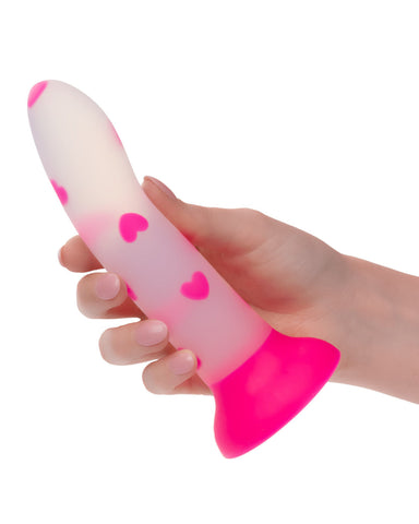 A hand holding a CalExotics Glow Stick Heart Silicone First Time Glow in the Dark Dildo, isolated on a white background.