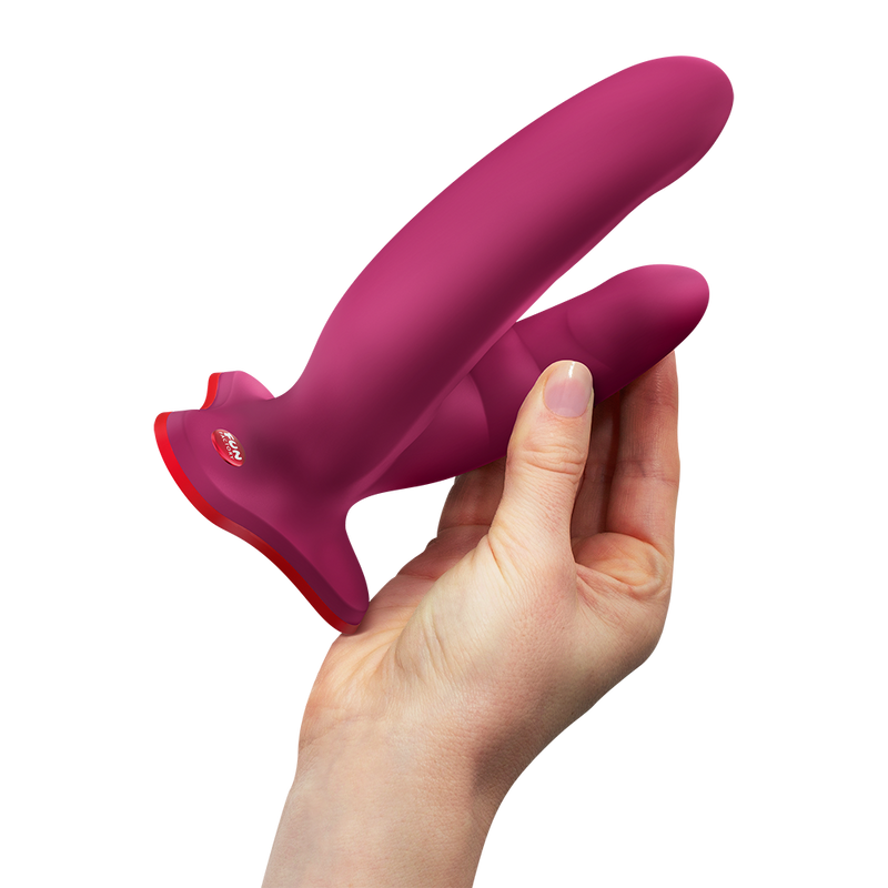 Hand holding a magenta silicone Fun Factory Ryde grinding dildo with a red suction base.