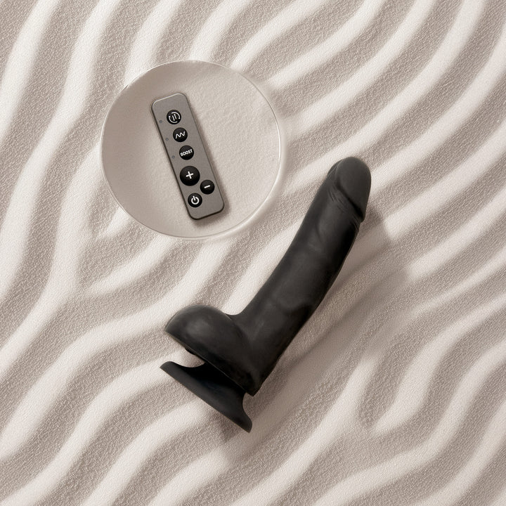 Black rotating vibrating realistic dildo with remote control on a textured surface.