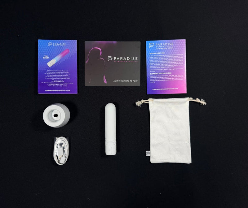 White Illumination Bullet LED vibrator, charging cable, stand, storage pouch, and Paradise Pleasure Products instructions.