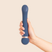 A hand holds the Hot & Cold Temperature-Changing G-Spot Massager, a blue cylindrical silicone massager with rounded ends, against a plain beige background.