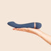 A hand holds the Hot & Cold Temperature-Changing G-Spot Massager, a sleek dark blue silicone vibrator with a metallic accent, designed for temperature play, against a plain beige background.