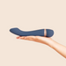A hand holds the Hot & Cold Temperature-Changing G-Spot Massager, a sleek dark blue silicone vibrator with a metallic accent, designed for temperature play, against a plain beige background.