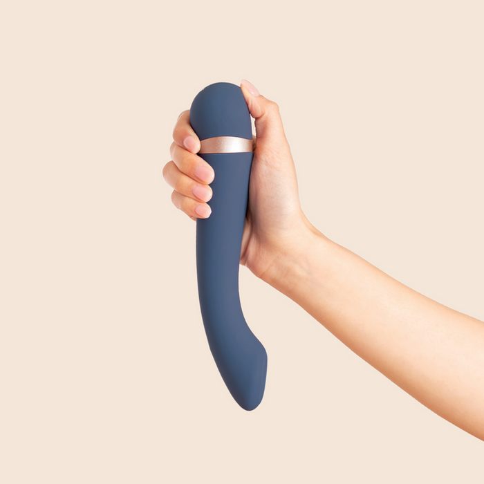 A hand holds the Hot & Cold Temperature-Changing G-Spot Massager, a blue silicone vibrator with a silver accent, against a plain beige background.