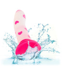 A Pink Glow Stick Heart Silicone First Time Glow in the Dark Dildo by CalExotics, with heart patterns splashing into water, causing droplets to scatter around, against a white background.