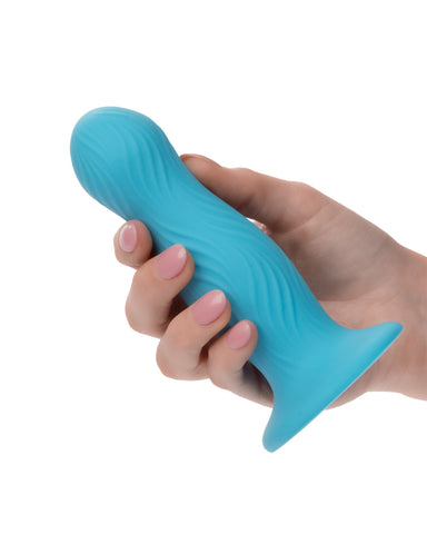 A person's hand with pink nail polish holding a blue, wavy-shaped suction cup CalExotics Wave Rider Swell Short, Girthy 5 Inch Liquid Silicone Dildo against a white background.