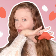 Woman in lace top holding a small, red, S-curve Pockety vibrator with a heart-wing tip.