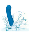 A Wave Rider Ripple First Time G-Spot and Prostate silicone dildo from CalExotics with a wavy texture splashes into water, causing dynamic water droplets to scatter around it against a white background.