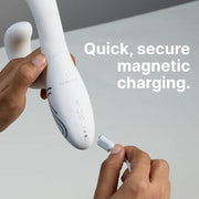 Hands connecting a white magnetic charging cable to the base of a white silicone rabbit vibrator.