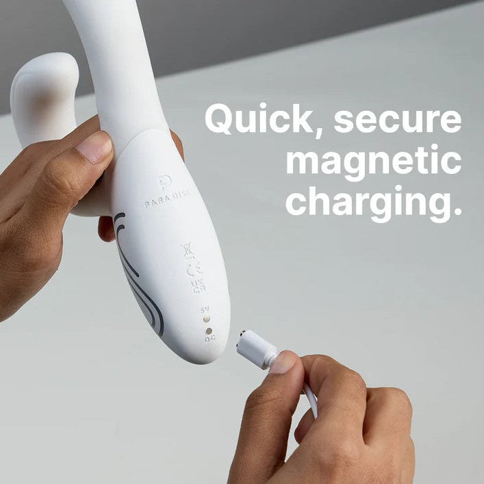 Hands connecting a white magnetic charging cable to the base of a white silicone rabbit vibrator.
