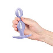 Hand holding a lavender silicone butt plug with a tapered tip, flared base, and two white oval inserts.
