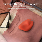 Orange Pockety palm vibrator on a folded pink sweater in an open suitcase with sunglasses.