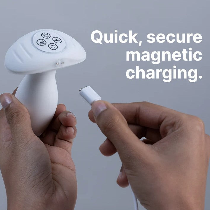 Hands holding a white mushroom-shaped LED butt plug and its magnetic charging cable.
