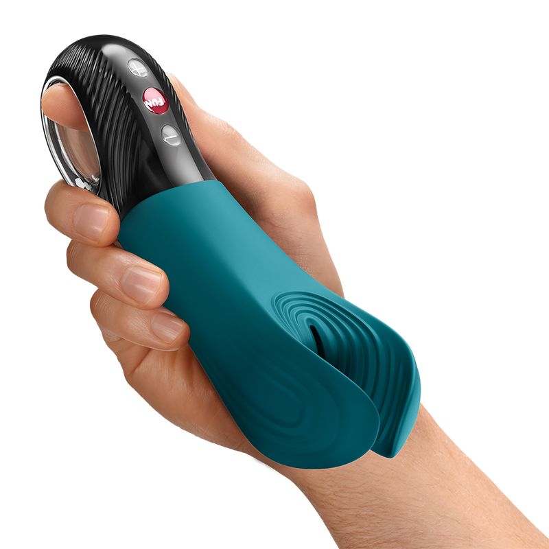 Hand holding a teal silicone Fun Factory Manta penis stroker with a black textured handle and red control buttons.