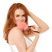 A woman with long red hair smiles at the camera, holding the Peaches 'n Cream Wrist Feather Tickler near her face while wearing a white satin camisole, inviting playful sensory exploration against a white background.