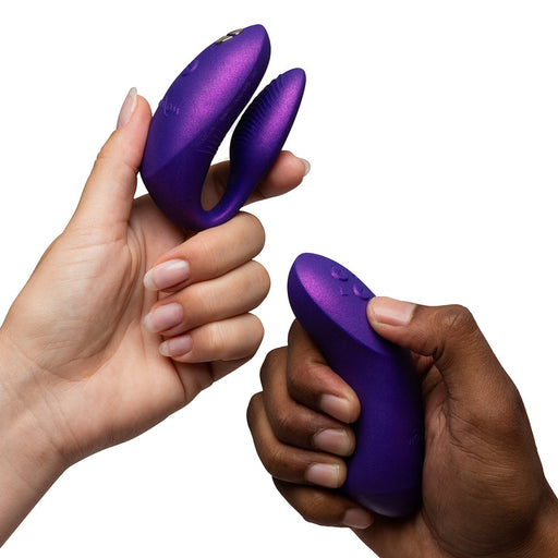 Two hands hold the We-Vibe Chorus Pro Wearable Couples' Vibrator with triple motors and its matching remote against a white background, showcasing its modern design and intimate G-spot stimulation for partners.