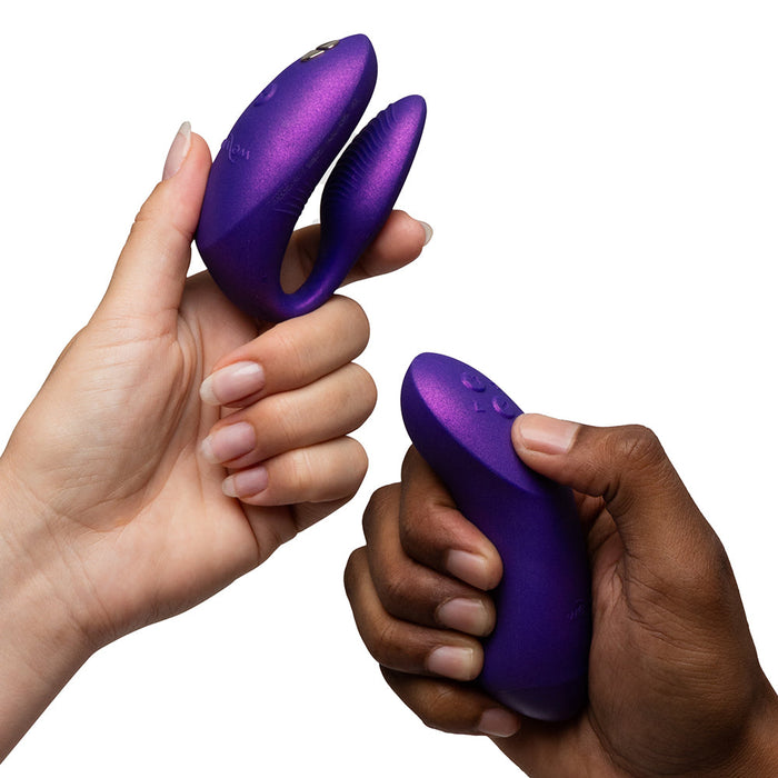 Two hands hold the We-Vibe Chorus Pro Wearable Couples' Vibrator with triple motors and its matching remote against a white background, showcasing its modern design and intimate G-spot stimulation for partners.
