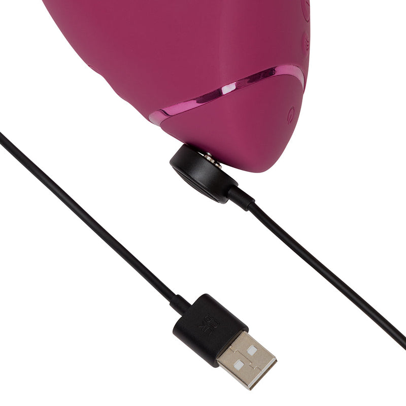 A close-up of the Womanizer Next Duo Pleasure Air + Vibration Blended Orgasm Stimulator being charged with a black USB cable connected to its charging port.