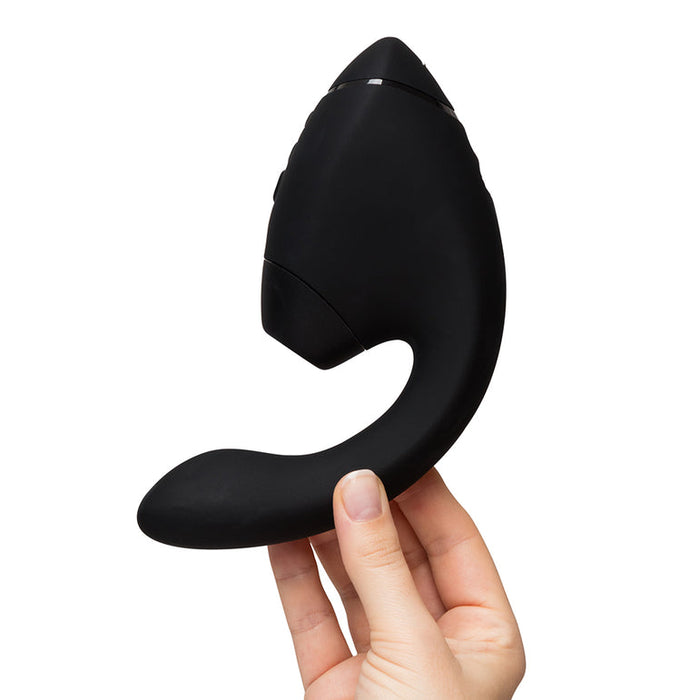 A hand holds the Womanizer Next Duo, a sleek black Pleasure Air + Vibration Blended Orgasm Stimulator designed for ultimate satisfaction.