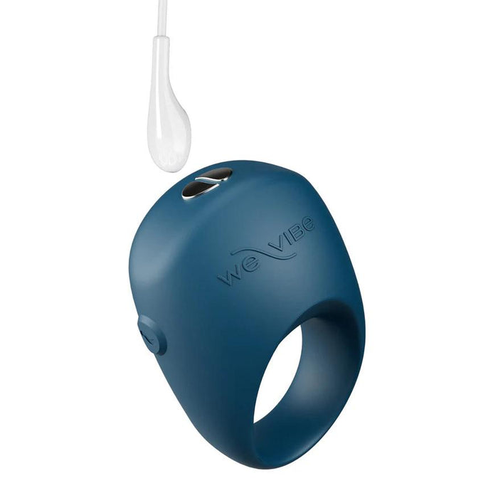 A blue We-Vibe Pivot 2 Vibrating Silicone Rechargeable Penis Ring with "We-Vibe" embossed, a control button, and a white charging cable inserted for hands-free clitoral stimulation.