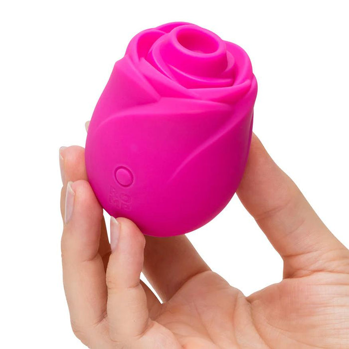 A hand holds the Romp Rose 2 Pleasure Air Clitoris Stimulator in pink—a compact, rechargeable silicone vibrator with a side button that offers discreet clitoral pleasure.