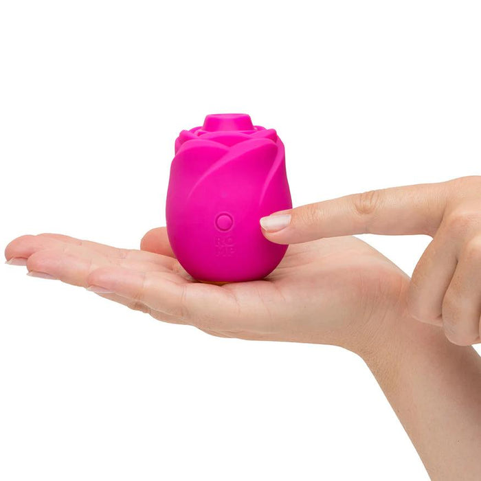 A hand holds the Romp Rose 2 Pleasure Air Clitoris Stimulator in pink while another hand points at it, highlighting interaction with this rechargeable silicone vibrator.