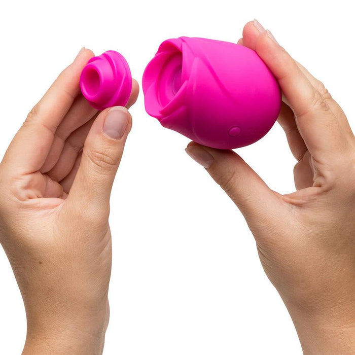 A person holds the Romp Rose 2 Pleasure Air Clitoris Stimulator in pink, showing its bright rose-shaped silicone body and detachable part against a plain white background.