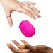 Two manicured hands, one light-skinned and one dark-skinned, reach toward the pink Romp Rose 2 Pleasure Air Clitoris Stimulator, shaped like a rose and floating against a white background.