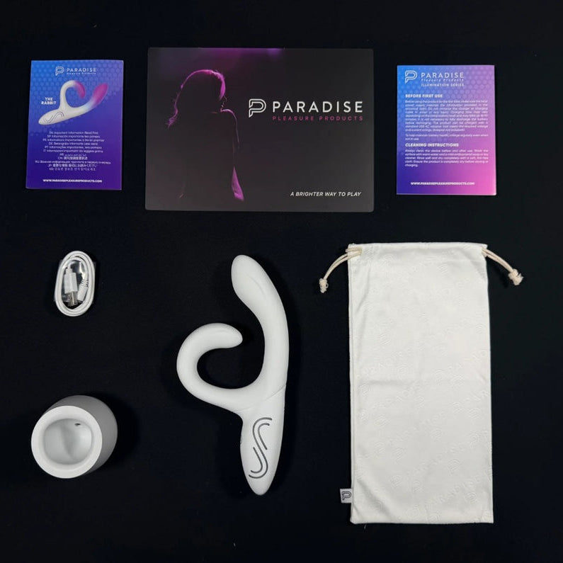White Illumination Rabbit LED vibrator, charging base, USB cable, storage bag, and Paradise Pleasure Products branding.