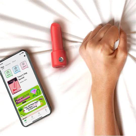 Red lipstick vibrator and a smartphone displaying the Monster Party app on a white sheet, with a hand clenching the sheet.