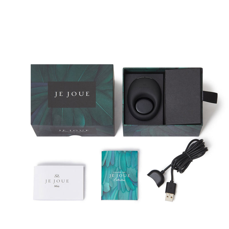 The Je Joue Mio Vibrating Cock Ring - Black boxed set includes the cock ring, USB charging cable, instruction manual, and a teal illustrated booklet, all beautifully displayed on a white background.